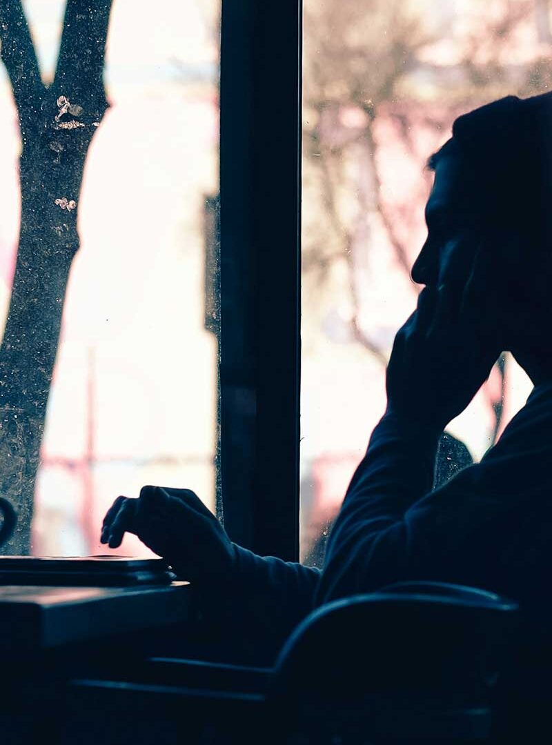 Silhouette of a person sitting in front of a laptop, backlit