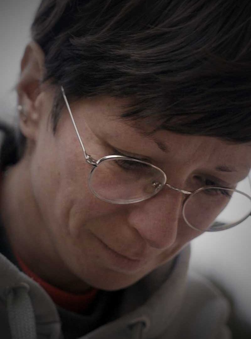 Nahaufnahme einer Frau mit kurzen dunklen Haaren und feiner Metallbrille, die den Blick senkt und leicht lächelt.