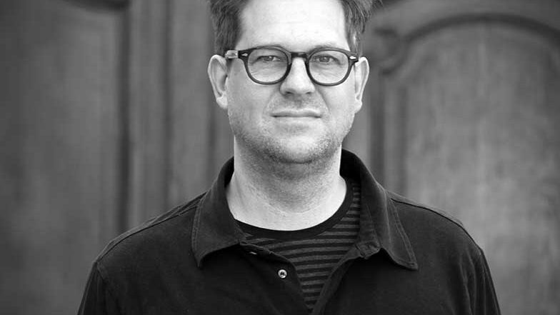 stefan-wolner-2025 Stefan Wolner, portrait in black and white in front of an old wooden door.