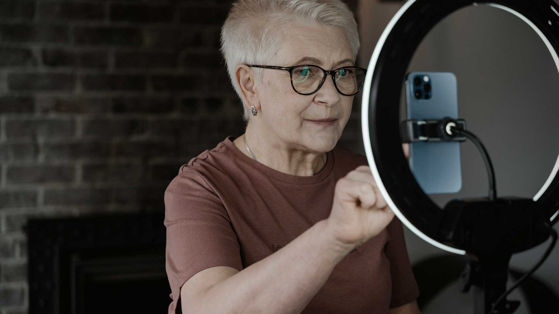 Elderly woman taking a selfie in front of a ring light.
