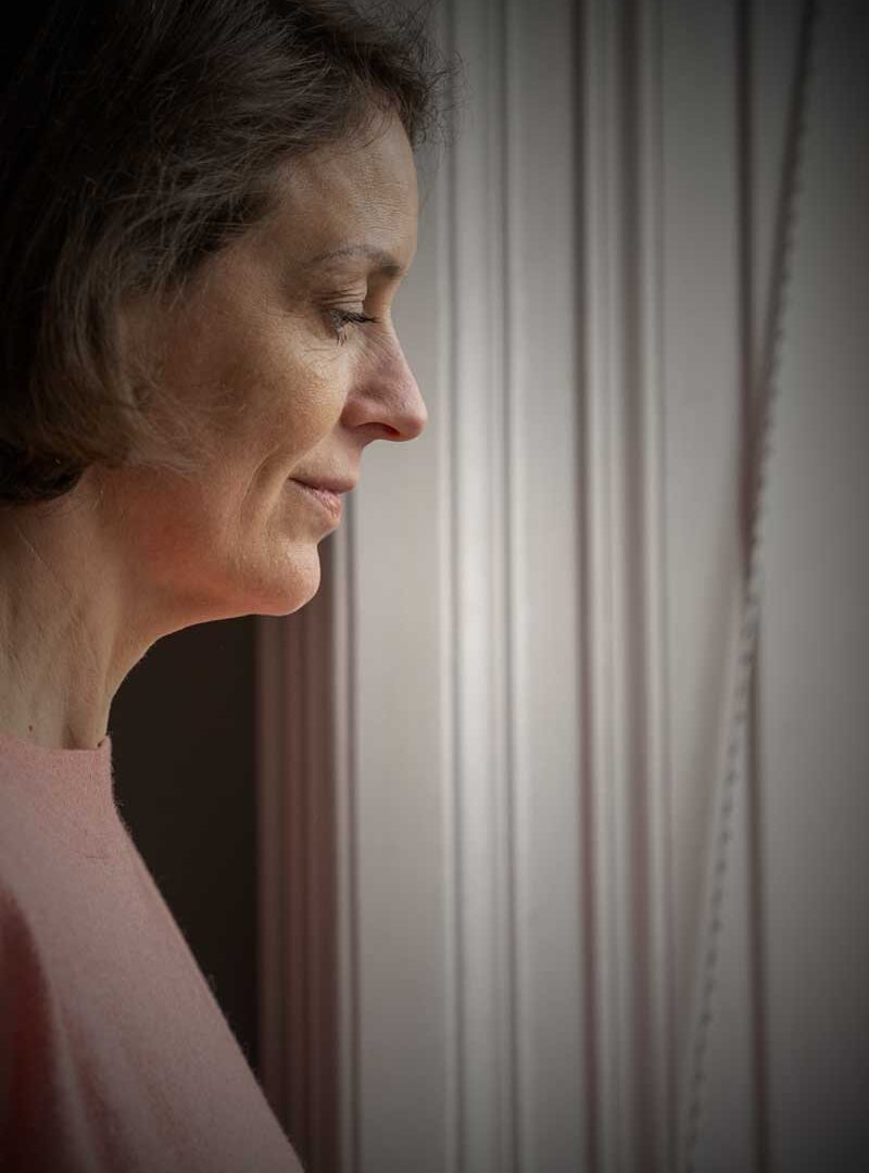 A woman in profile beside a curtain, looking down
