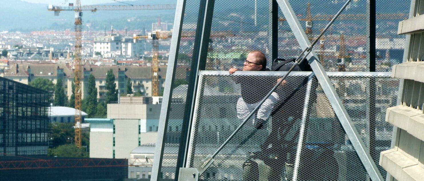 Martin Habacher im Elektrorollstuhl auf einem Steg hoch über Wien, im Hintergrund Baukräne.