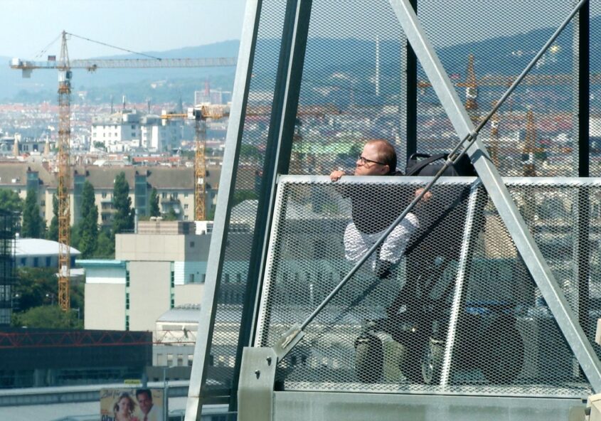 Martin Habacher im Elektrorollstuhl auf einem Steg hoch über Wien, im Hintergrund Baukräne.