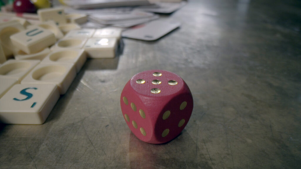 Homo Ludens – Still 03 A red die and game tiles on a table